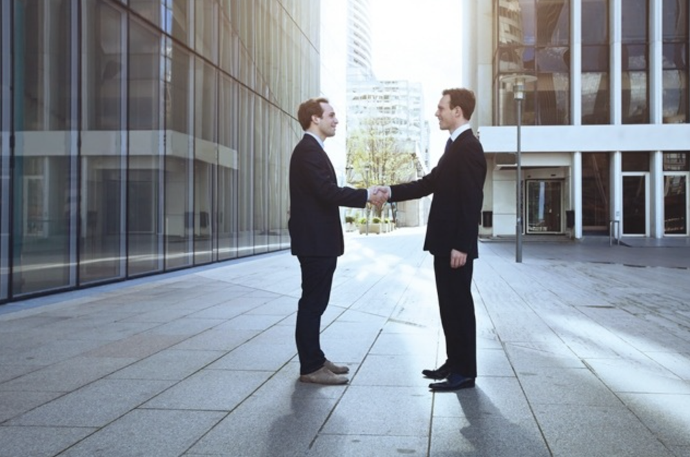 Twee managers staan tussen twee gebouwen en geven elkaar een zakelijke handdruk