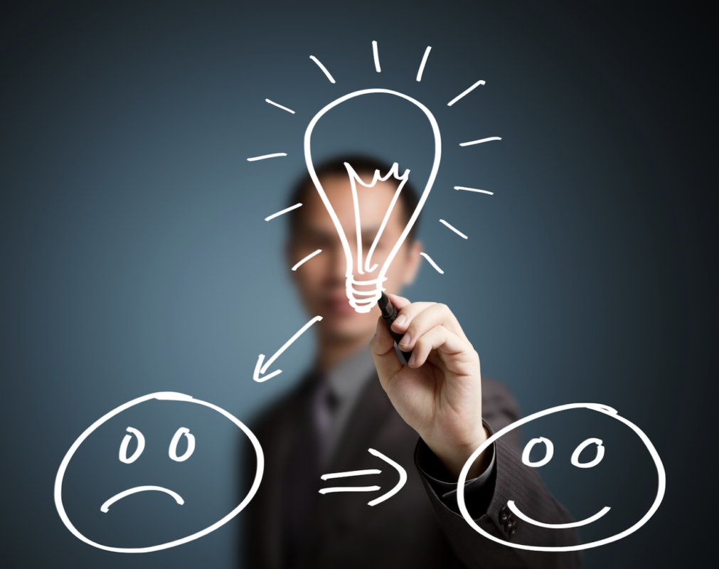 Een zakenman maakt een tekening op een whiteboard. We zien een brandende lamp dat wijst naar een gezicht met een droevig gezicht. Het droevig gezicht wijst naar een blij gezicht wat verandering aantoont.