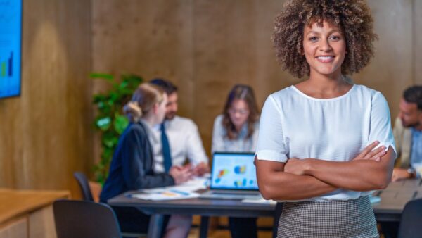 Projectleider staat met gekruiste armen voor tafel met collega's